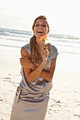 Reife blonde Frau mit silbernem Sommerkleid und orangener Blume am Strand
