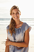 A mature blonde woman on a beach wearing a silver summer dress