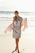 A mature blonde woman on a beach wearing a silver summer dress