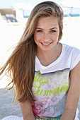 A young blonde woman on a beach wearing a colourful t-shirt