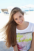 A young blonde woman on a beach wearing a colourful t-shirt