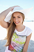 Junge blonde Frau mit buntem Shirt und weißem Sommerhut  am Strand