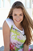 A young blonde woman on a beach wearing a colourful t-shirt