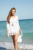 A young blonde woman a white summer hat on a beach wearing a white summer dress