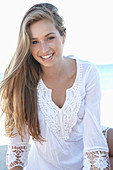 A young blonde woman on a beach wearing a white summer dress