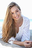 A young blonde woman on a beach wearing a white summer dress