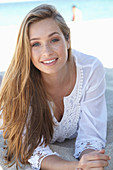 A young blonde woman on a beach wearing a white summer dress