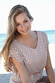 A young blonde woman on a beach wearing a beige polka-dot dress