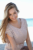 A young blonde woman on a beach wearing a beige polka-dot dress