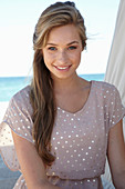 A young blonde woman on a beach wearing a beige polka-dot dress