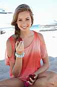 A young blonde woman on a beach wearing a salmon-coloured, off-the-shoulder top