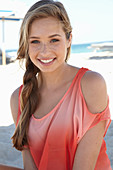 A young blonde woman on a beach wearing a salmon-coloured, off-the-shoulder top