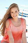 A young blonde woman on a beach wearing a salmon-coloured, off-the-shoulder top