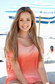 A young blonde woman on a beach wearing a salmon-coloured, off-the-shoulder top