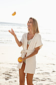 Reife blonde Frau mit Grapefruit in Dessous und Strickjacke am Strand