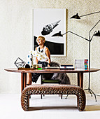 Blonde woman behind oval dining table, multi-arm floor lamp and leopard-look bench
