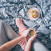A woman wearing bed socks, sitting an a bed wth cup of coffee and piece of cake