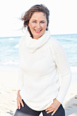 A brunette woman on a beach wearing a white knitted jumper