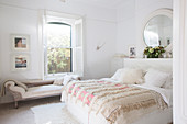 Double bed with bedspread and chaise longue in front of window in white bedroom