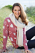 A brunette woman wearing a white scarf with a pink knitted jumper with hearts