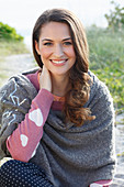 A brunette woman wearing a grey shawl and a pink knitted jumper with heats