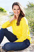 A brunette woman wearing a yellow jumper and jeans