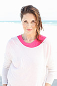 Brünette Frau in pinkfarbenem T-Shirt und weißem Pulli am Strand
