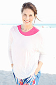 Brunette woman wearing pink T-shirt, white sweater and multicoloured trousers on beach