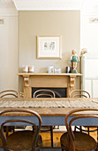 Bistro chairs at wooden table in front of open fireplace in beige wall