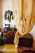 Künstlerisch gestalteter Vorhang, dahinter Designer-Jacke an der Wand und Vintage Nähmaschine auf Kommode
