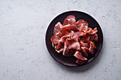 Thin ham slices on wooden plate on white concrete background
