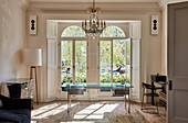 Glass table below chandelier in bright study with Victorian French windows