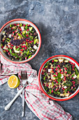 Kale, pomegranate and feta cheese tabbouleh in two bowls with spring onions and lemon mint dressing
