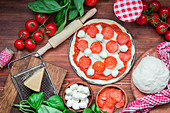 Ungebackene Salamipizza und Zutaten auf Holztisch