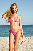 Junge blonde Frau im rosa Bikini am Meer