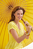 A young brunette woman wearing a yellow shirt holding a parasol