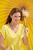Junge brünette Frau im gelben Shirt hält Sonnenschirm
