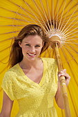 A young brunette woman wearing a yellow shirt holding a parasol