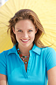 A young brunette woman wearing a blue shirt in front of a yellow parasol