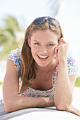 A young brunette woman outside wearing a colourful summer dress with sunglasses on her head