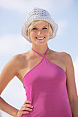 A mature blonde woman with short hair on a beach wearing a purple top and striped bikini bottoms