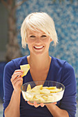 A mature blonde woman with short hair wearing a blue top with a bowl of pineapple