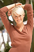 A mature blonde woman with short hair outside wearing a brown top