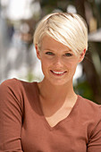 A mature blonde woman with short hair outside wearing a brown top