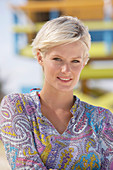 A mature blonde woman with short hair on a beach wearing a patterned summer dress