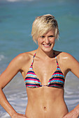 A mature blonde woman with short hair on a beach wearing a striped bikini