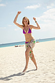 Junge blonde Frau im lila Bikini mit Strandtuch um die Hüften am Strand