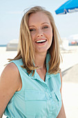 A young blonde woman on a beach wearing a light-blue summer dress