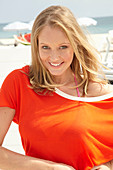 A young blonde woman on a beach wearing a purple bikini and an orange top