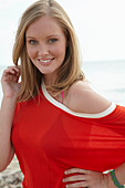 A young blonde woman on a beach wearing a purple bikini and an orange top